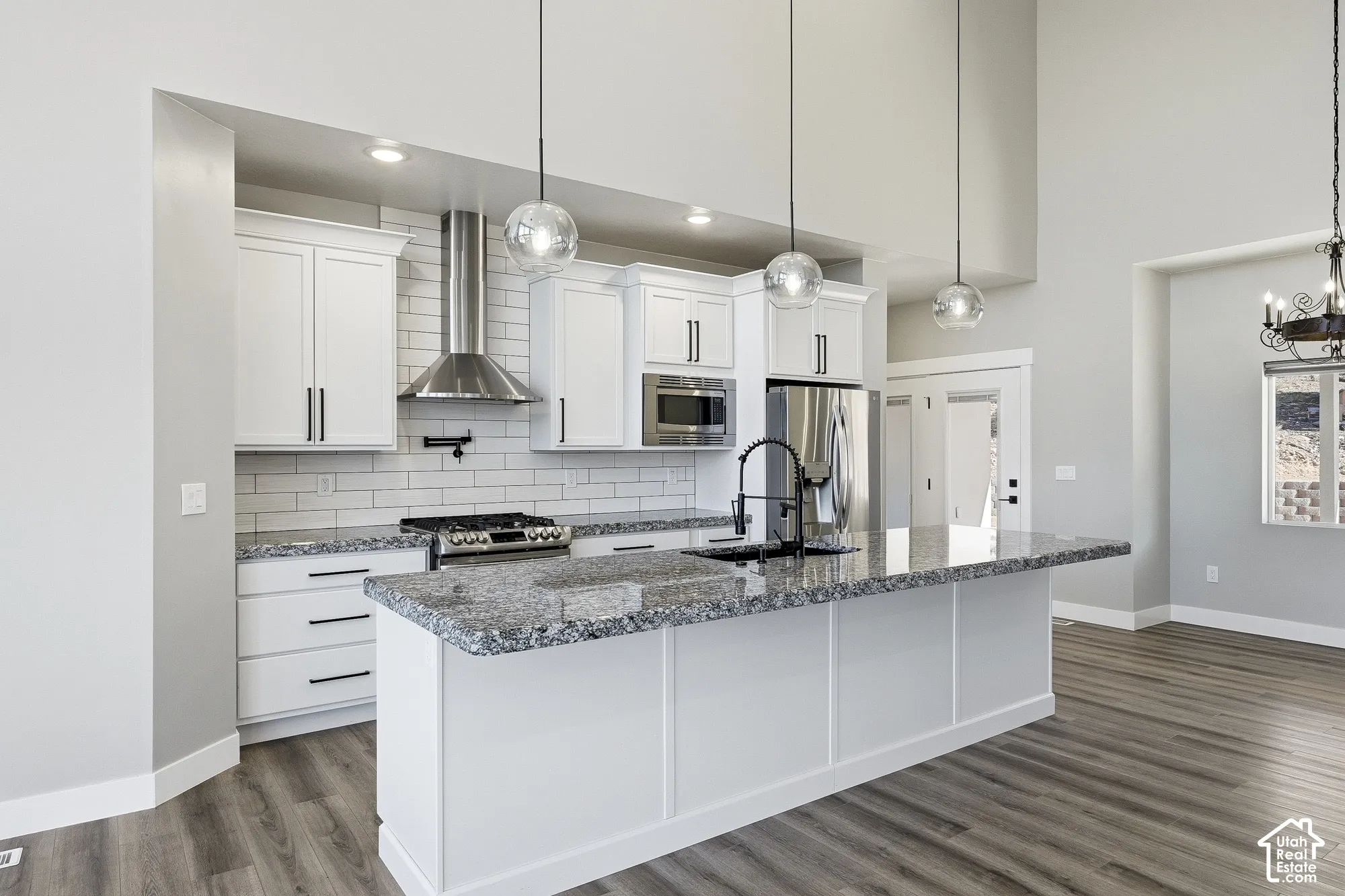 Kitchen featuring a large island with a stone-finish countertop, white cabinetry, stainless steel appliances, and wood-finish flooring