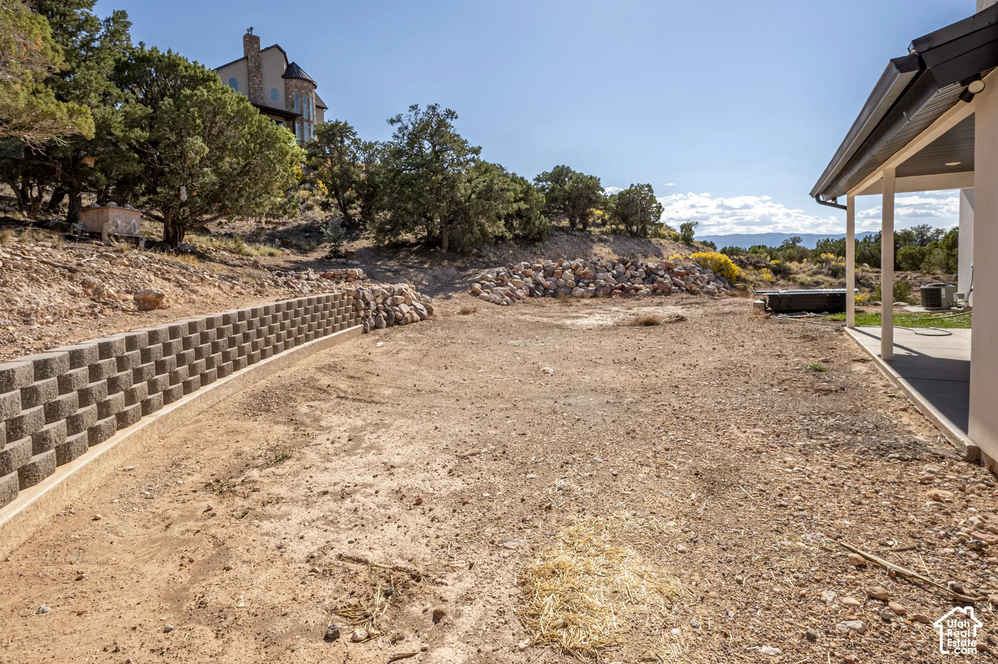 Expansive property featuring a concrete block retaining wall and a covered patio area