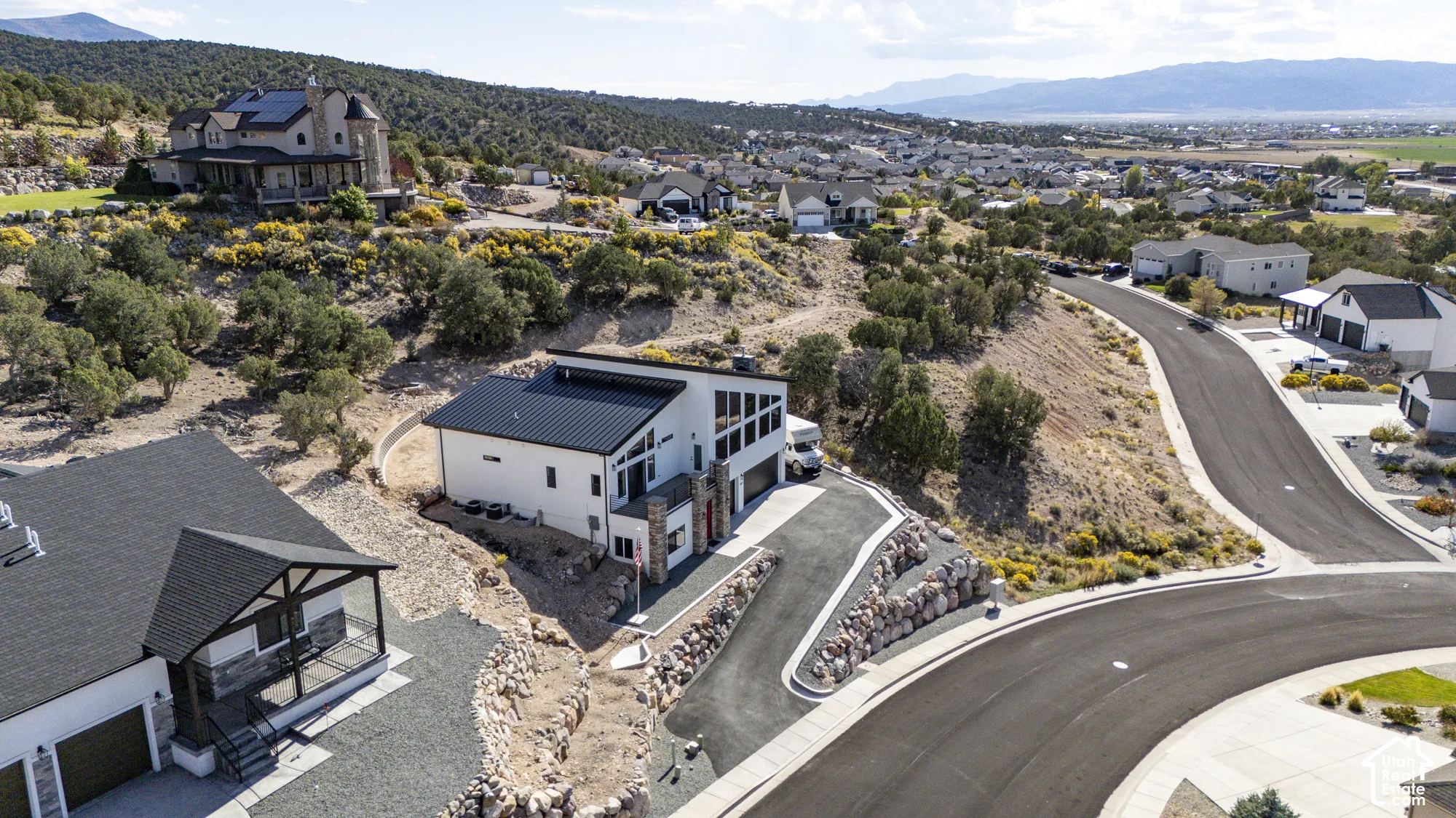 Modern residential architecture with a black metal roof, white siding, and stone accents