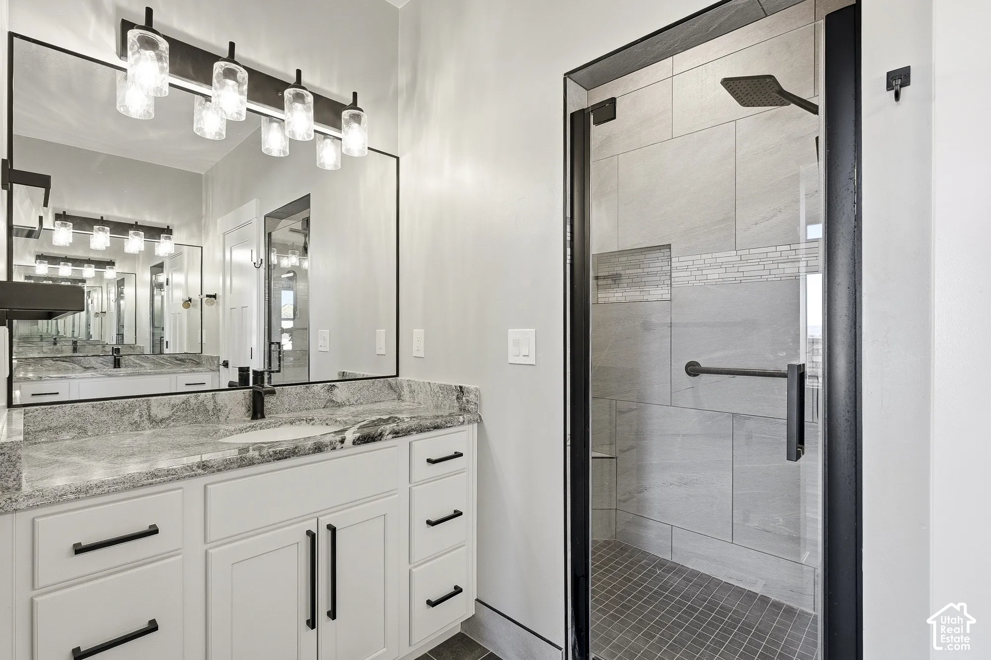 Dual vanity with stone countertop, white shaker-style cabinetry, and matte black hardware