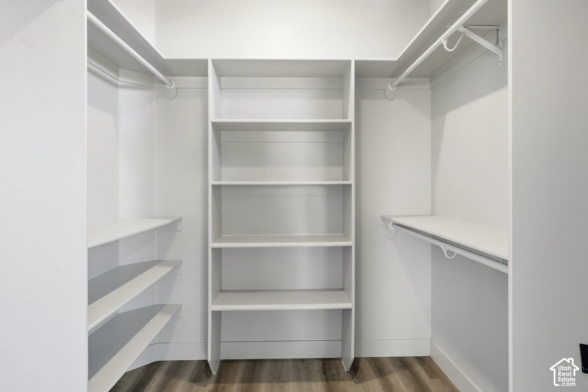 Closet featuring integrated shelving, multiple hanging rods, and wood-finish flooring