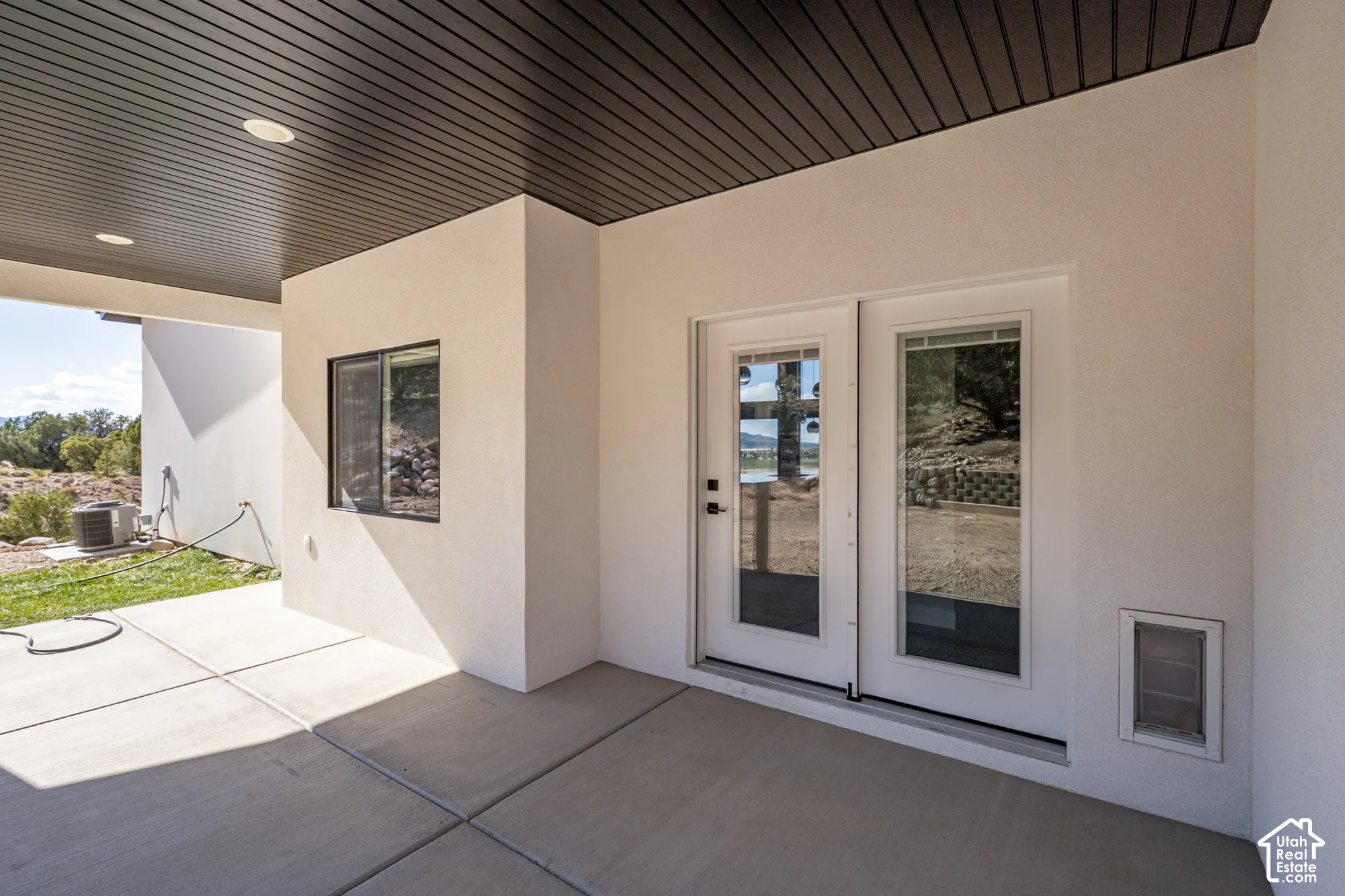 Covered concrete patio with recessed lighting, black slatted ceiling, and white double glass-panel doors