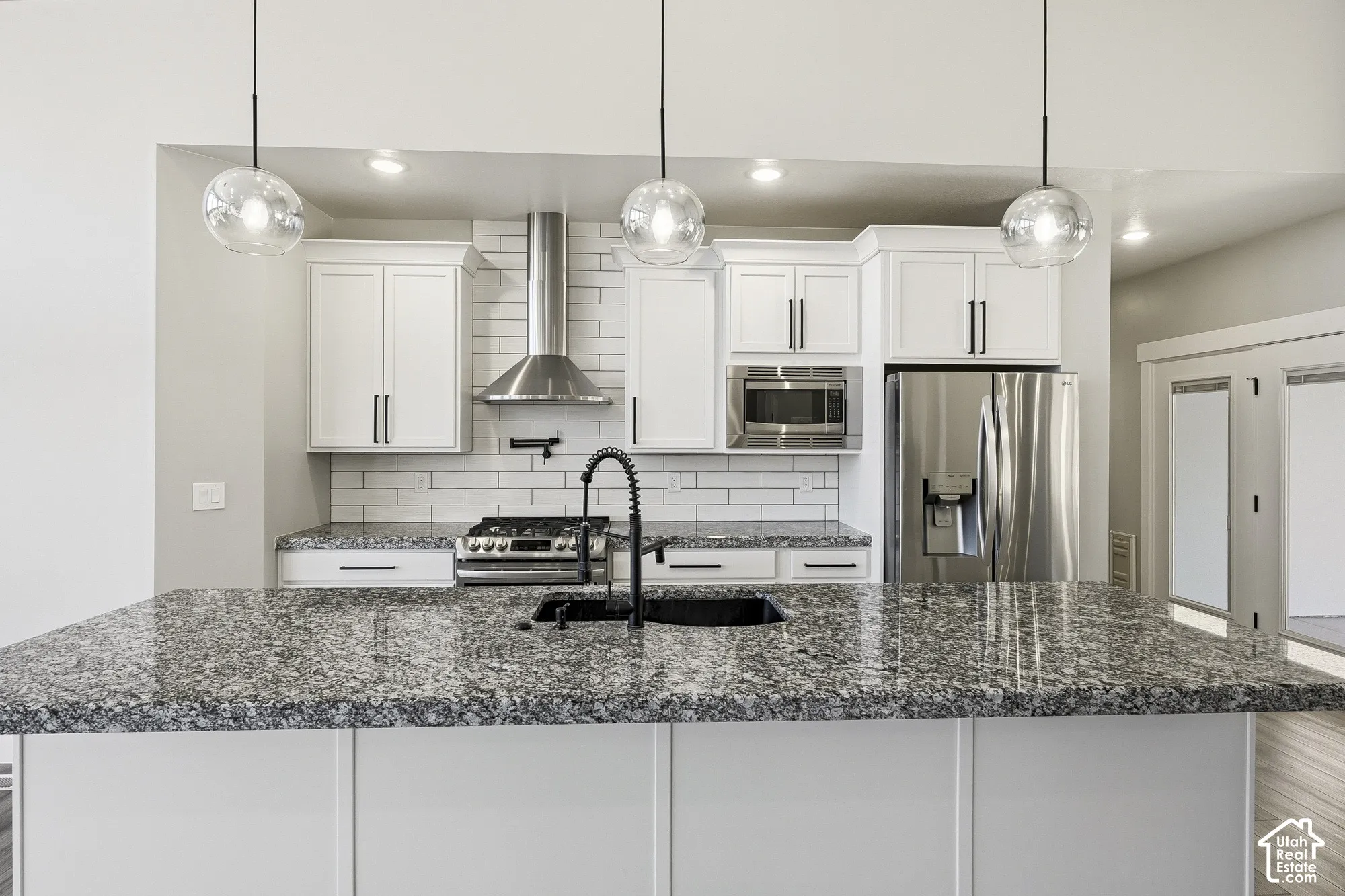Kitchen featuring white cabinetry, subway tile backsplash, stainless steel appliances, granite countertops, and pendant lighting