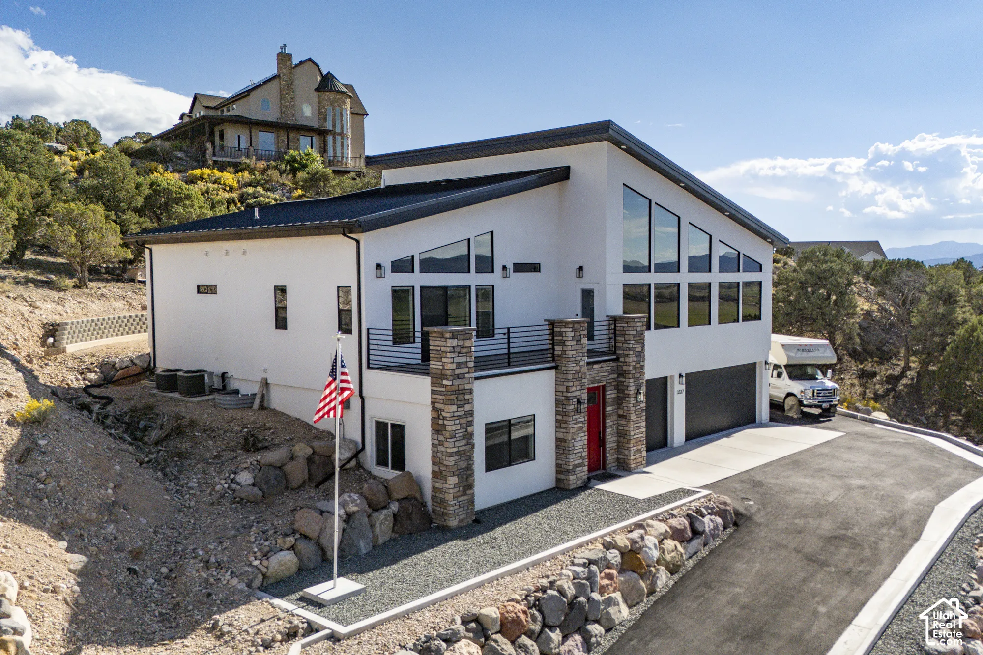 Contemporary white exterior with extensive angular windows, black-framed balcony, stone veneer columns, a bright red front door, and an attached two-car garage