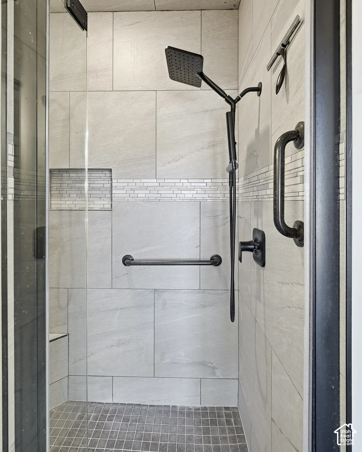 Shower enclosure featuring large format wall tiling, a decorative mosaic tile accent, a built-in shower niche, a square rain showerhead, and a built-in shower bench