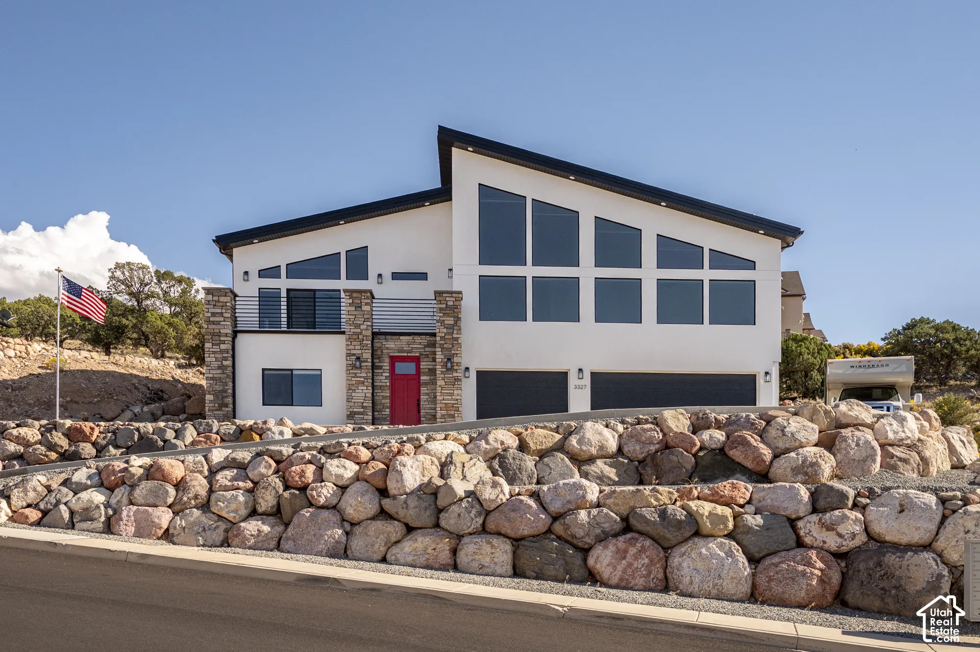 Contemporary exterior with a distinctive roofline, stone facade accents, expansive windows, a bright red entry door, and a two-car garage