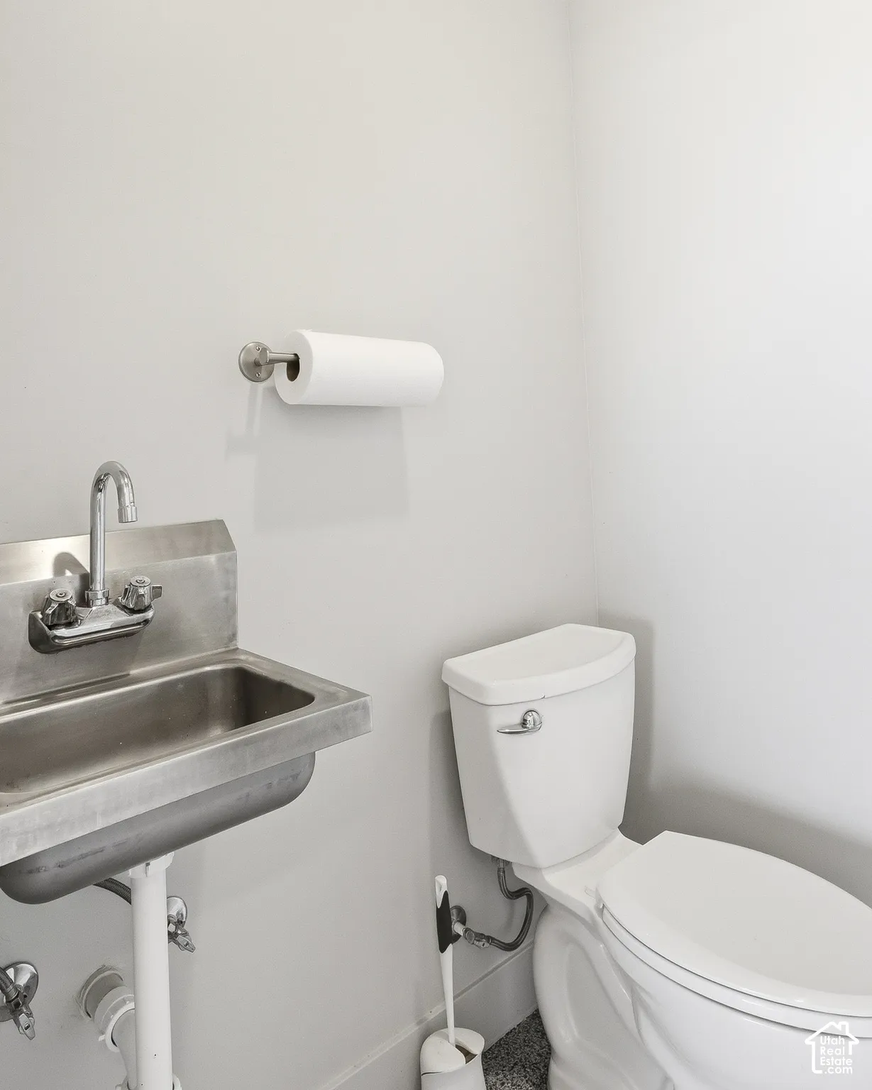 Wall-mounted paper towel holder, commercial-grade stainless steel sink, dual-handle faucet, and a two-piece toilet