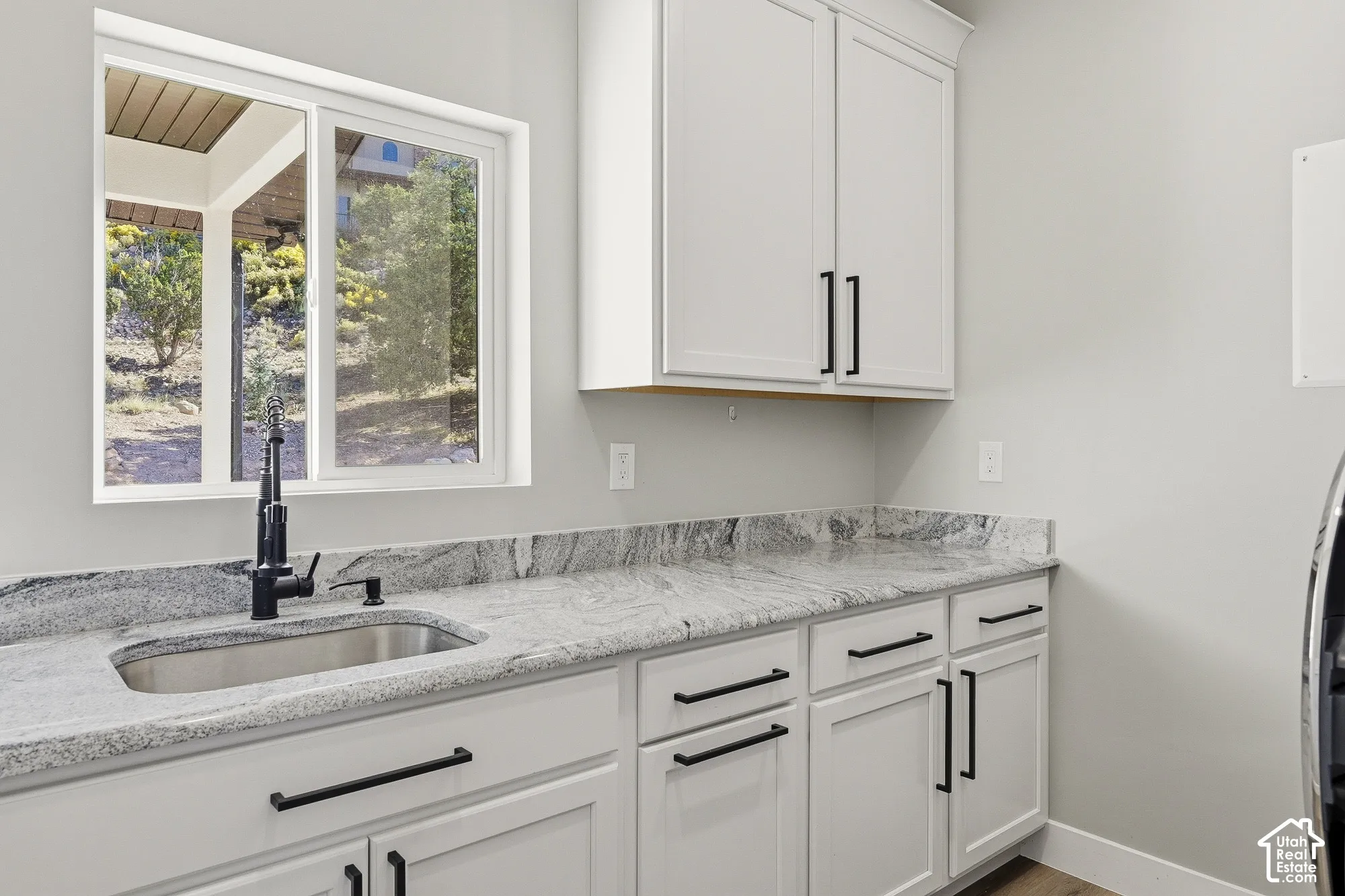 White cabinetry with matte black hardware, light-toned stone finish countertops, and a stainless steel sink with a matte black faucet