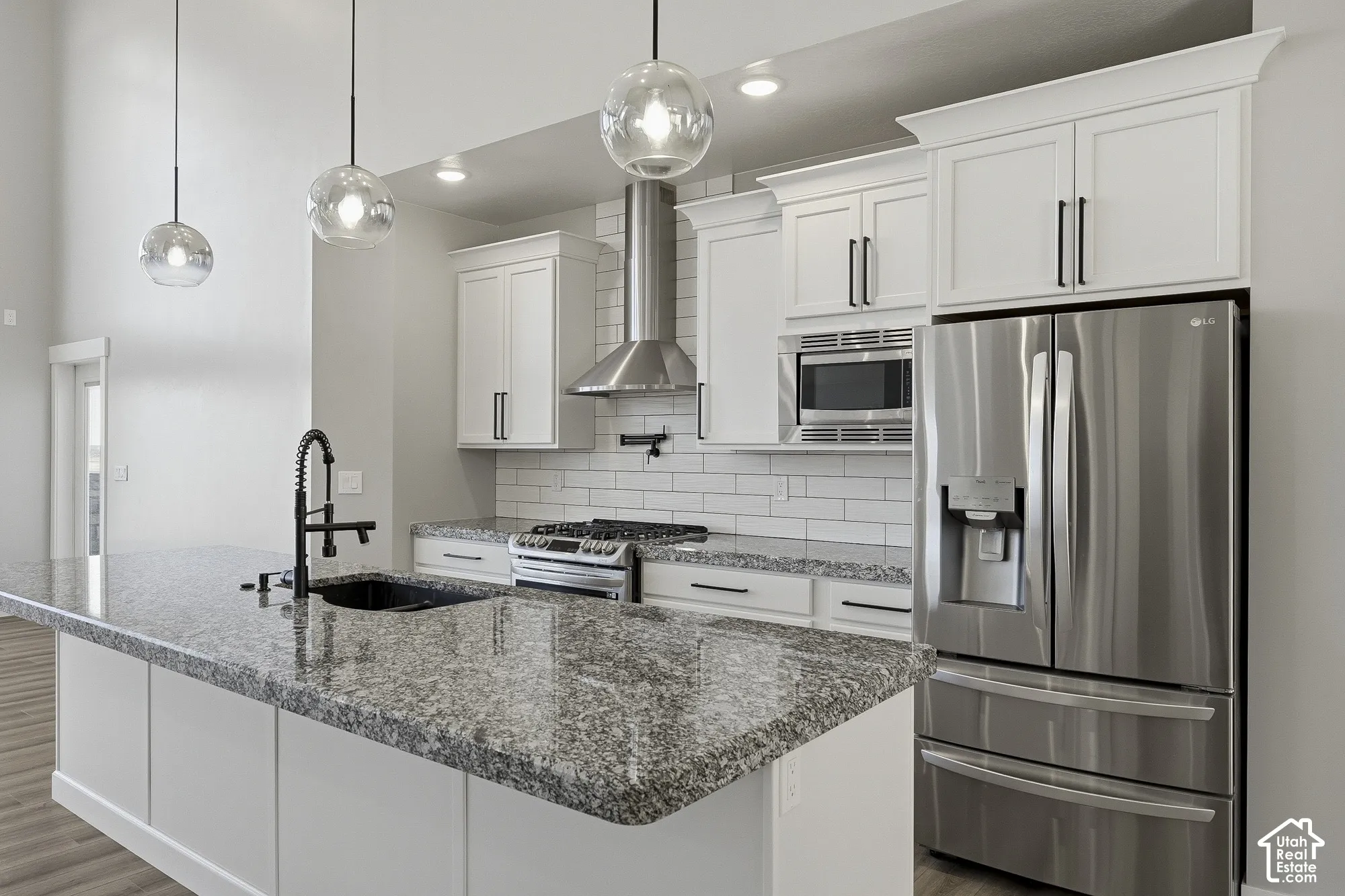 Kitchen featuring a granite-top island with an undermount sink, white cabinetry with dark hardware, stainless steel appliances, and a subway tile backsplash