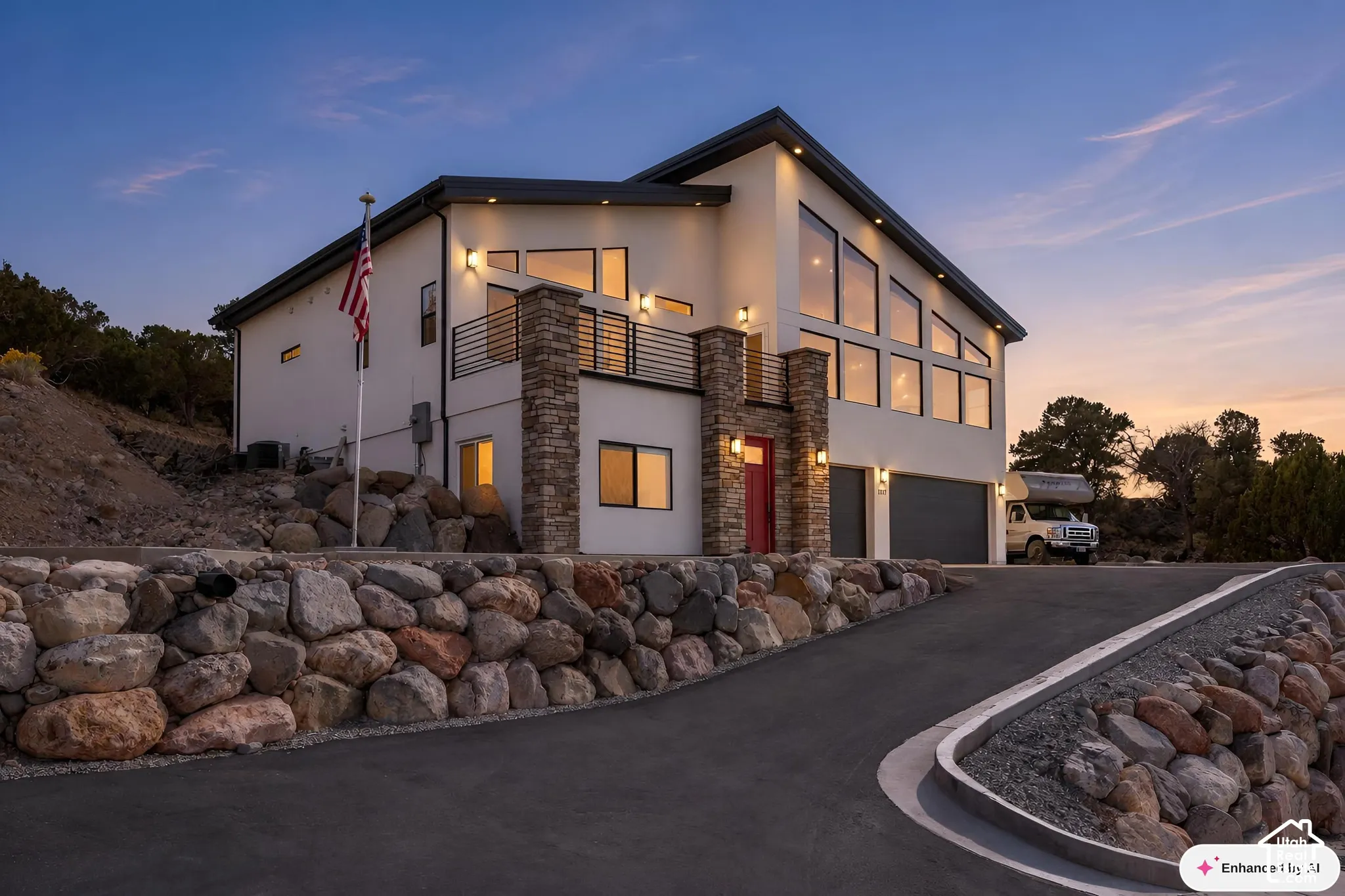 Contemporary residence featuring a stone-clad facade, multi-level exterior balcony with horizontal railings, extensive floor-to-ceiling windows, and paved driveway with integrated stone retaining walls