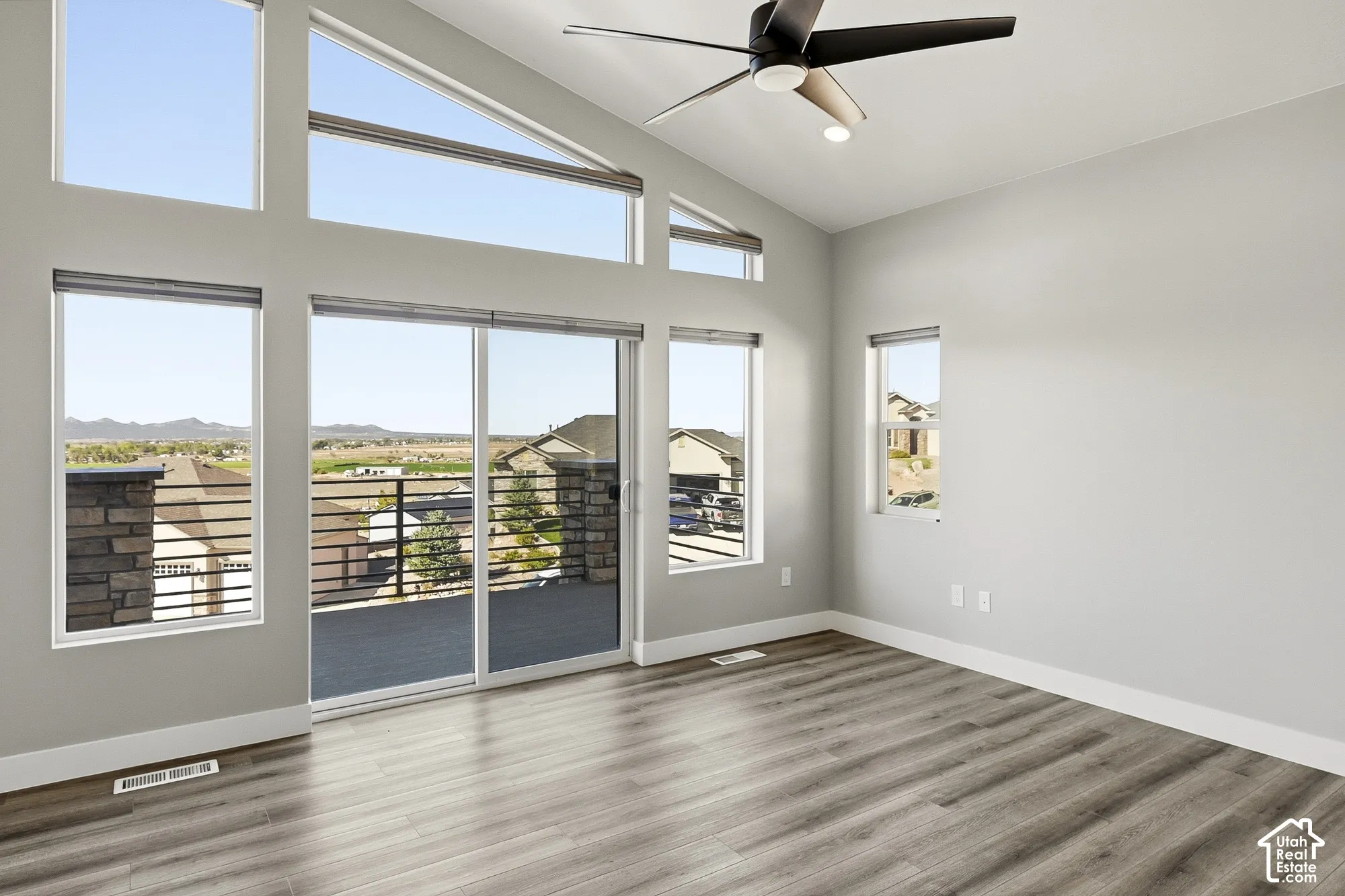 Vaulted ceiling, wood-finish flooring, ceiling fan with integrated lighting, multiple windows, and sliding glass door to exterior deck