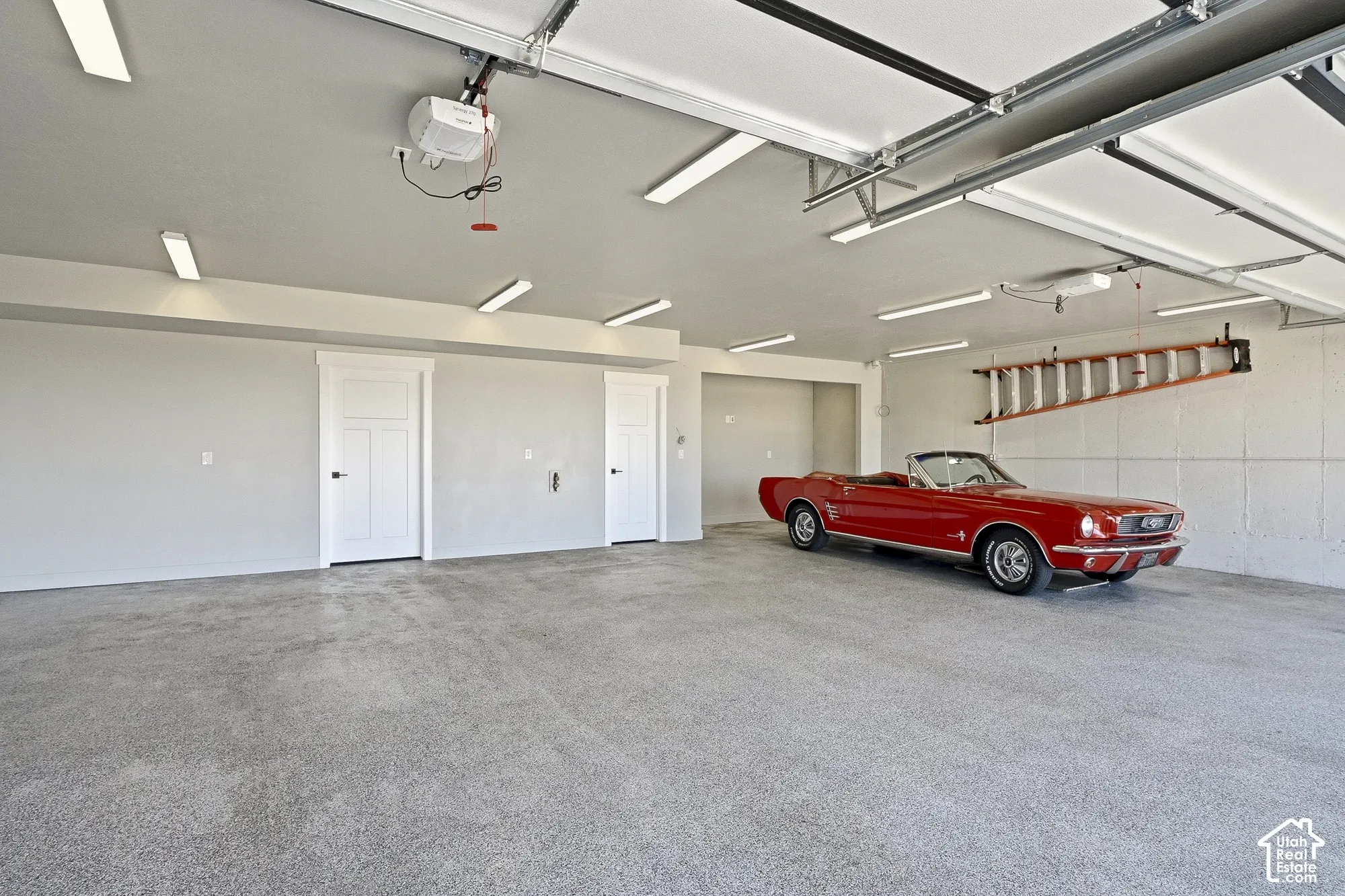 Spacious garage featuring a finished floor, multiple overhead lights, and two interior access doors with dark hardware