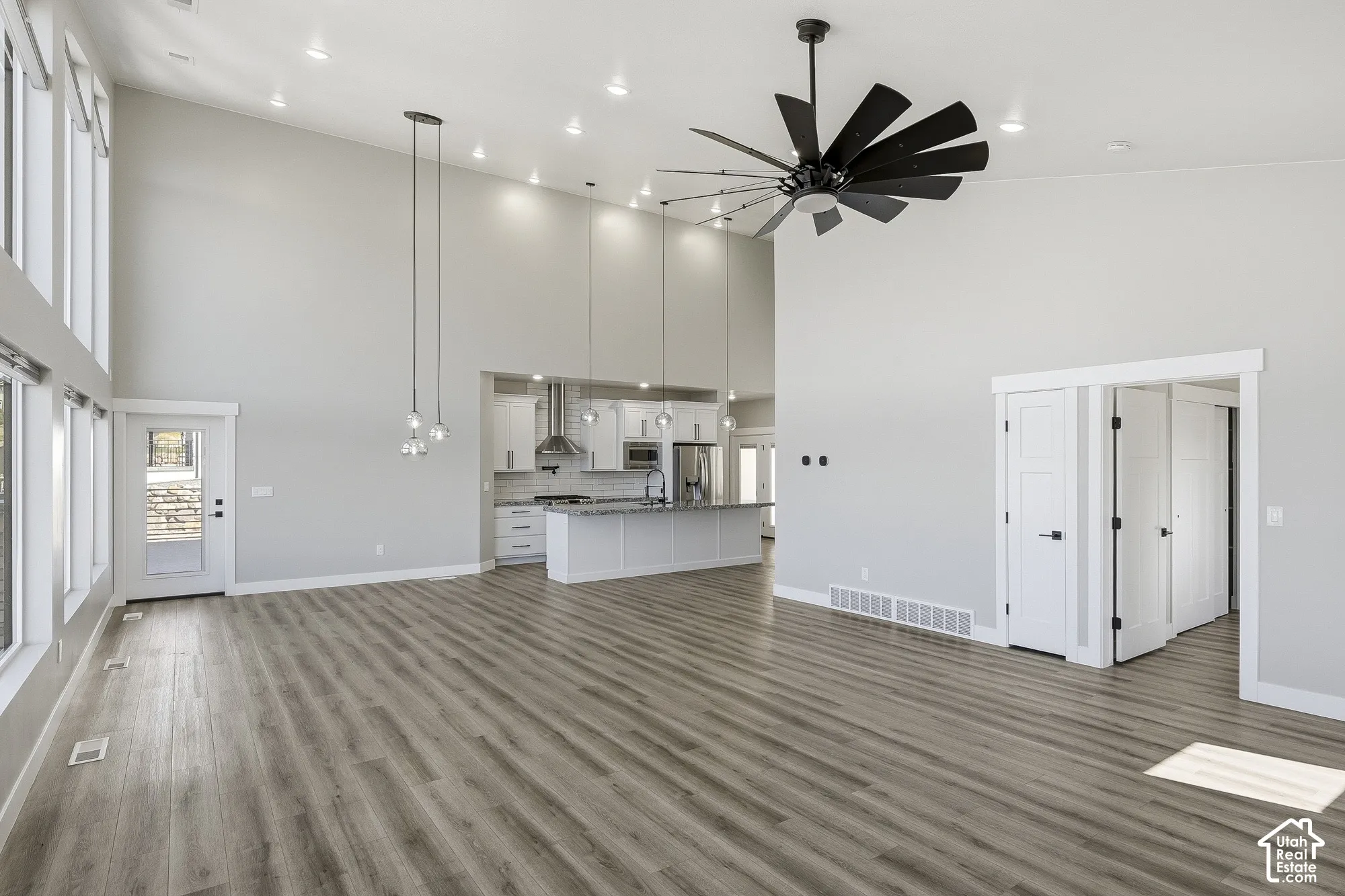 Vaulted ceilings with recessed lighting, large picture windows, wood-finish flooring, modern ceiling fan, and a kitchen featuring a central island with countertop seating