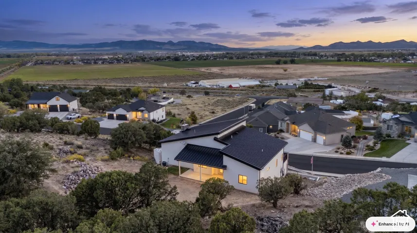 Aerial perspective featuring a multi-level residence with a metal roof, concrete driveway, attached garage, and covered patio, set against a mountain backdrop