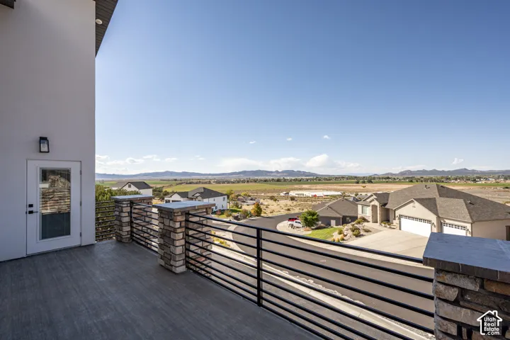 Upper-level balcony featuring plank-style flooring, a glass-paned door, and modern horizontal railings with stone pillars