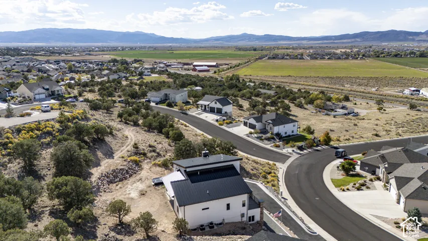 Contemporary residence with a black metal roof and white exterior, positioned on a paved road with an expansive natural landscape