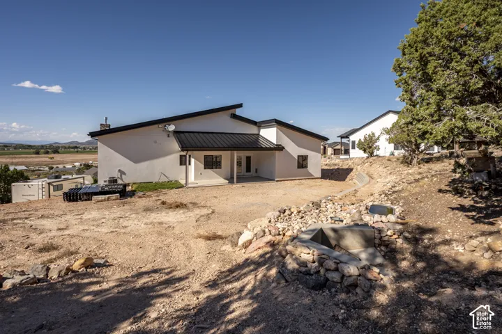 White stucco exterior with a black metal roof, featuring multiple windows and a covered patio area