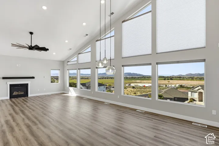 Vaulted ceilings, expansive windows, wood-finish flooring, recessed lighting, and a modern fireplace with a white mantel and dark hearth