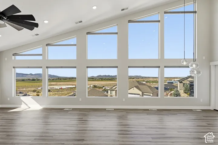 Vaulted ceiling with recessed lighting, expansive multi-pane windows, wood-finish flooring, contemporary ceiling fan, and pendant light fixture