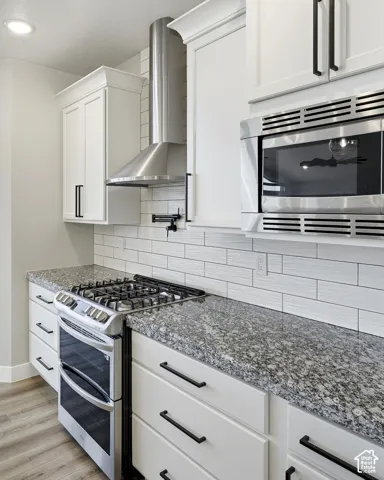 White shaker-style cabinetry with matte black hardware, stainless steel gas range with double oven, stainless steel microwave, stone countertops, and white subway tile backsplash