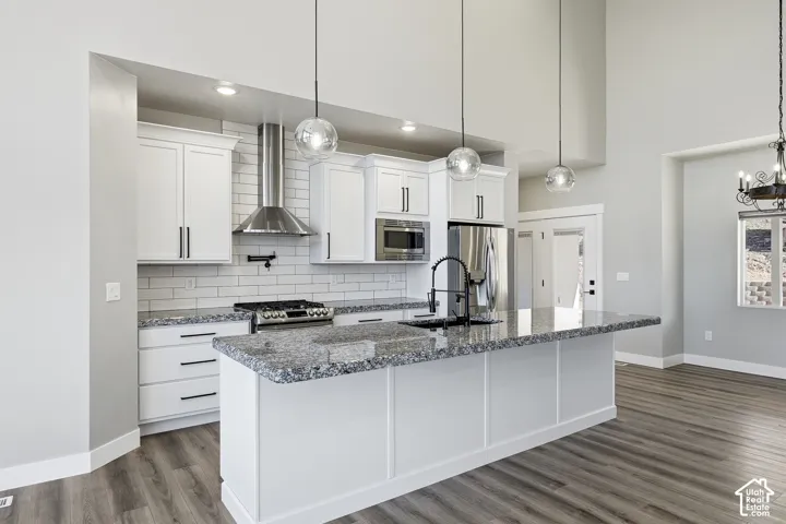 Kitchen featuring a large island with a stone-finish countertop, white cabinetry, stainless steel appliances, and wood-finish flooring