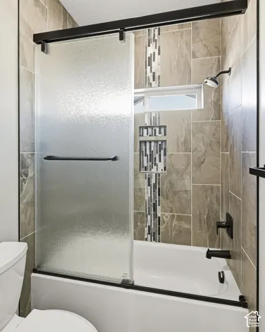 Tub-shower combination featuring a sliding textured glass door, matte black fixtures, and a tiled surround with a decorative mosaic accent