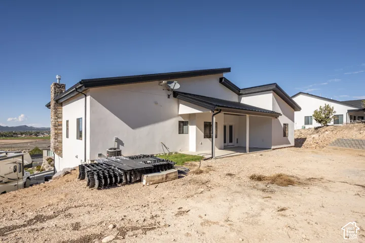 Exterior featuring a white stucco finish, black sloped roof, covered patio, and a stone chimney