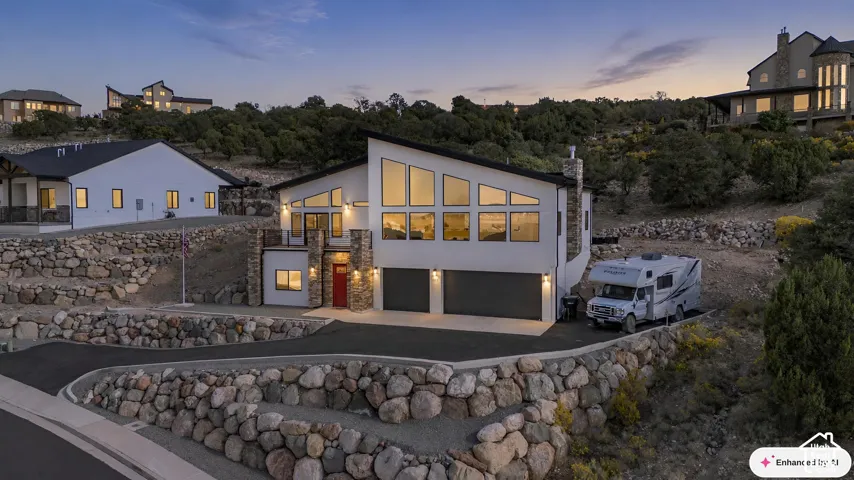 Contemporary multi-level exterior featuring stacked stone accents, expansive geometric windows, a two-car garage, and terraced stone retaining walls