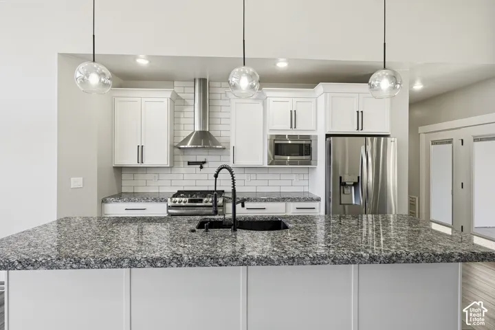 Kitchen featuring white cabinetry, subway tile backsplash, stainless steel appliances, granite countertops, and pendant lighting
