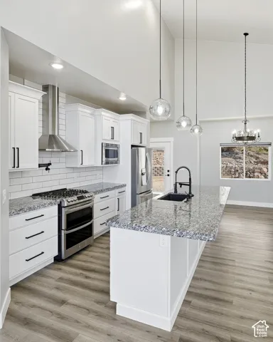 Vaulted ceiling with pendant lighting, white cabinetry with black hardware, stainless steel appliances, speckled stone countertops, and wood-finish flooring