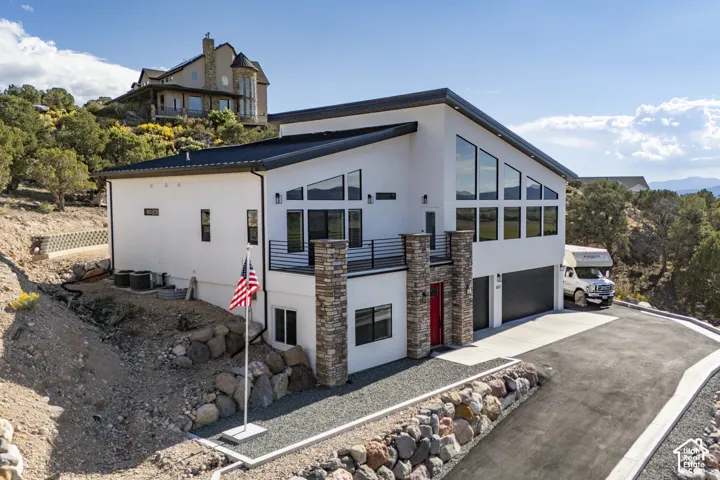 Contemporary white exterior with extensive angular windows, black-framed balcony, stone veneer columns, a bright red front door, and an attached two-car garage