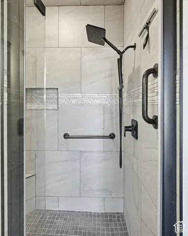 Shower enclosure featuring large format wall tiling, a decorative mosaic tile accent, a built-in shower niche, a square rain showerhead, and a built-in shower bench