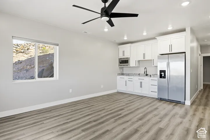 Open-concept living area featuring wood-finish flooring, a white kitchen with stainless steel appliances, white cabinetry, and recessed lighting