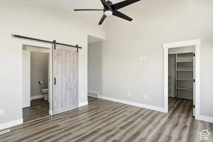 Vaulted ceiling with a black ceiling fan, wood-finish flooring, white walls, and a wood-finish barn door