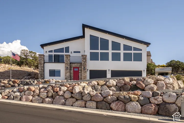 Contemporary exterior with a distinctive roofline, stone facade accents, expansive windows, a bright red entry door, and a two-car garage