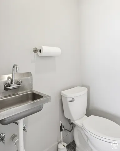 Wall-mounted paper towel holder, commercial-grade stainless steel sink, dual-handle faucet, and a two-piece toilet