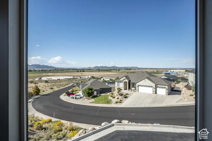 Expansive territorial scenery with distant mountains, a curved paved street, and residential structures with attached garages