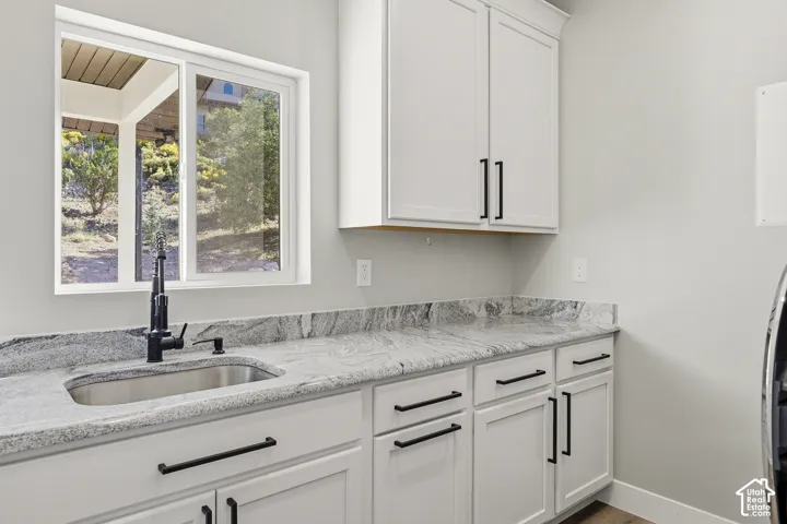White cabinetry with matte black hardware, light-toned stone finish countertops, and a stainless steel sink with a matte black faucet