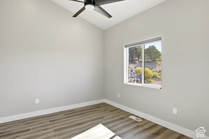 Vaulted ceiling, wood-finish flooring, ceiling fan, and a window with roller shades