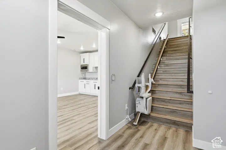 Wood-finish flooring throughout, white cabinetry with dark hardware, built-in microwave, light-toned countertops, and a stair lift