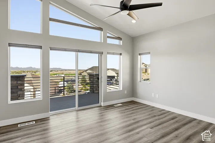 Vaulted ceiling, wood-finish flooring, ceiling fan with integrated lighting, multiple windows, and sliding glass door to exterior deck