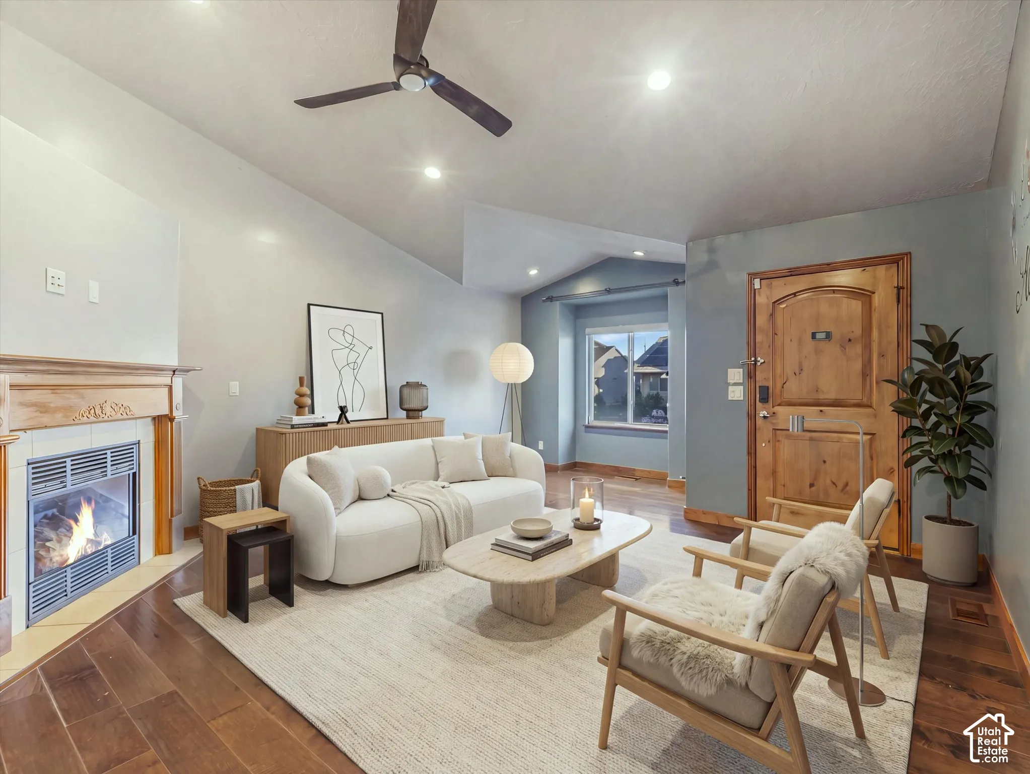 Vaulted ceiling, wood-finish flooring, recessed lighting, gas fireplace with wood mantel, and a solid wood entry door with arched paneling. Digitally Staged.