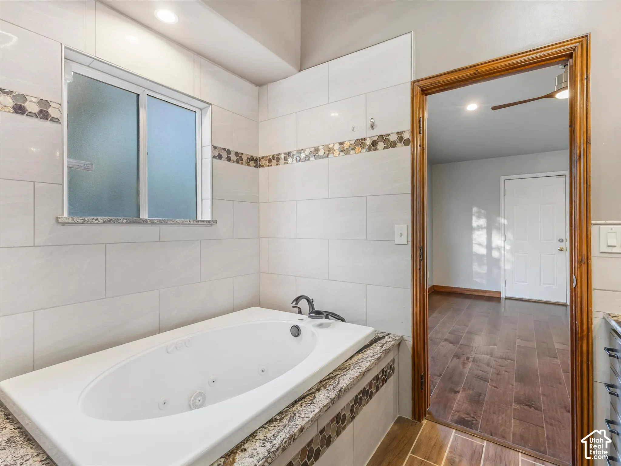 Built-in jetted tub with tiled surround, decorative mosaic tile accents, and a frosted window