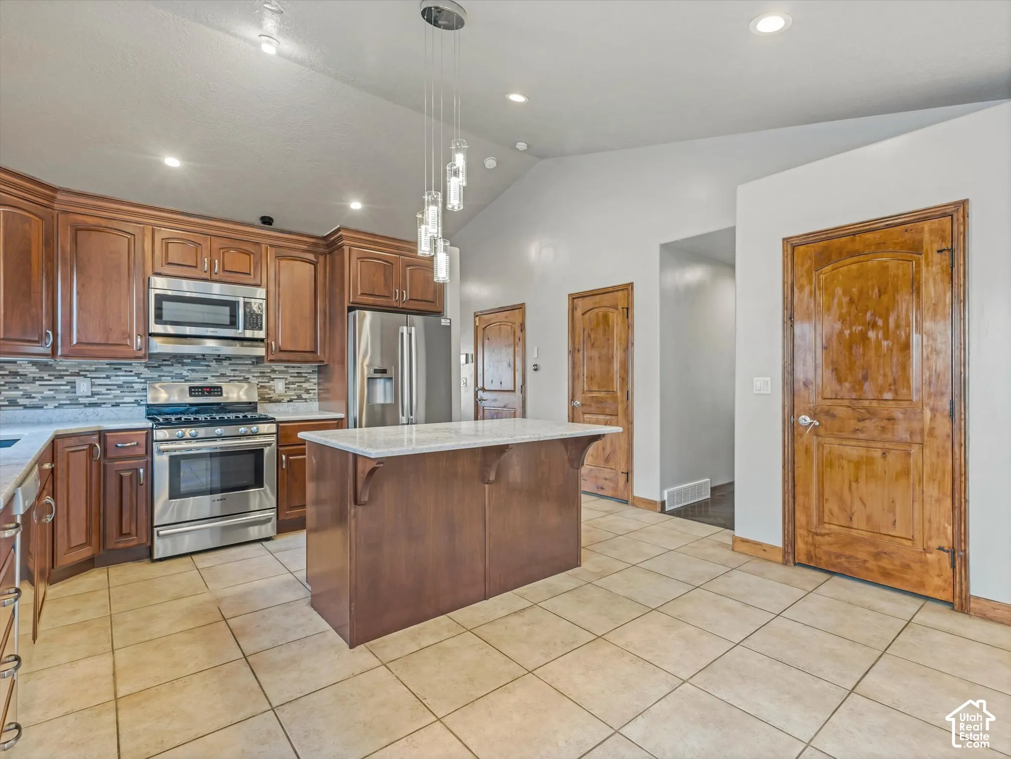 Kitchen featuring a center island with a light-toned countertop, stainless steel appliances, wood cabinetry, and tile flooring