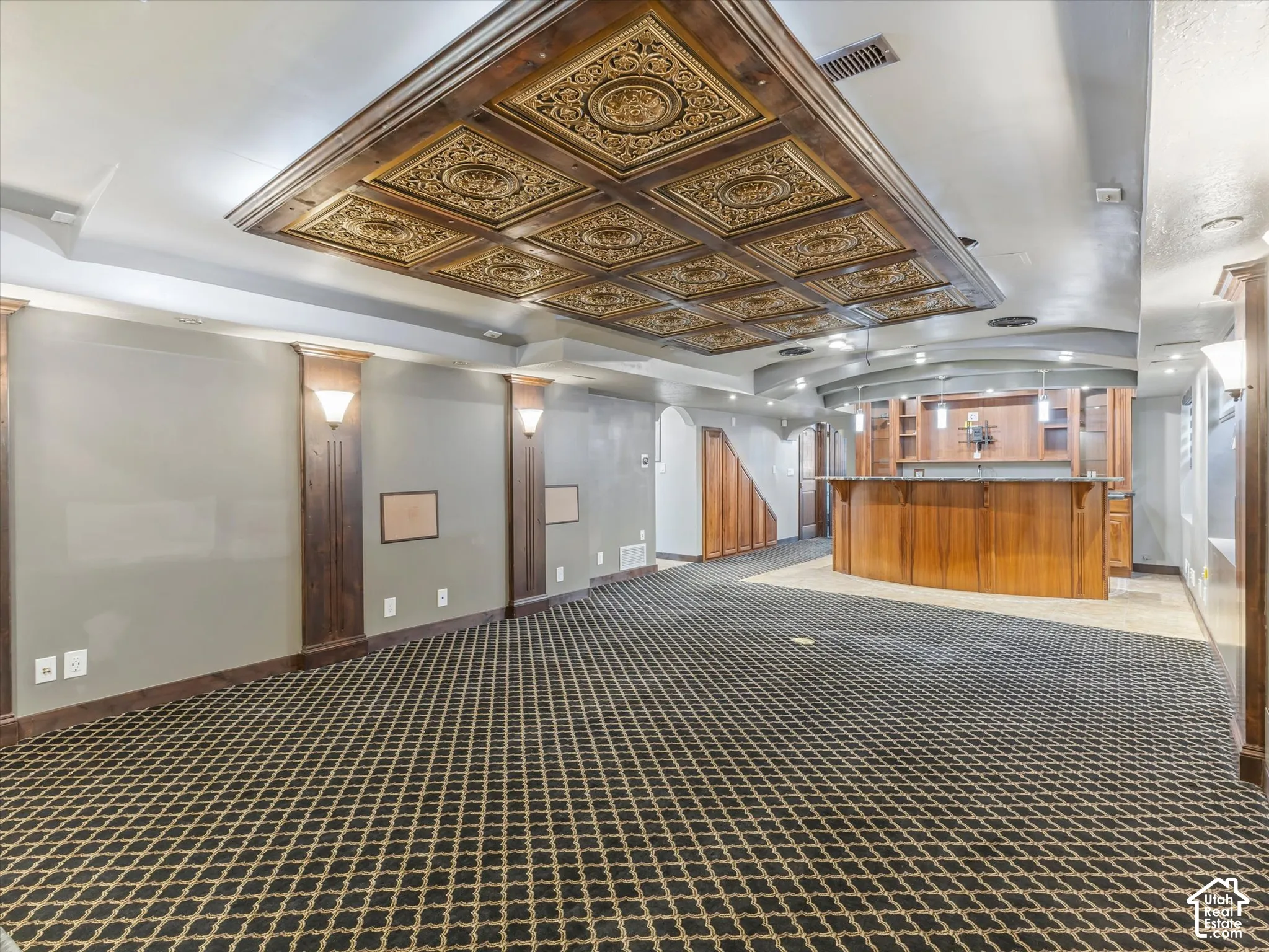 Recessed ceiling with decorative panels, built-in wet bar with wood cabinetry, patterned carpeting, and integrated wall sconces