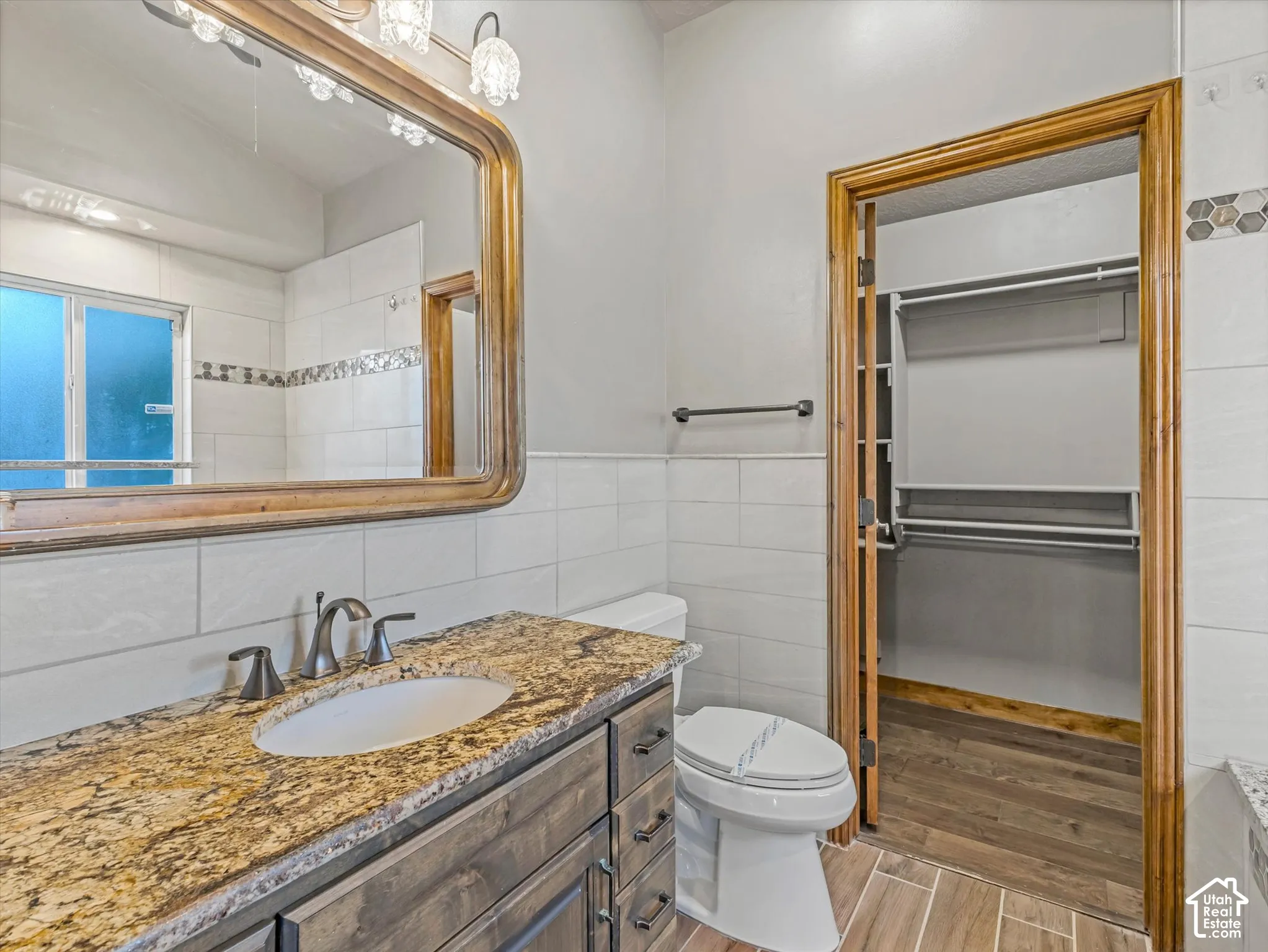 Vanity with an undermount sink and stone countertop, wood-finish cabinet, wall-mounted light fixture, and large framed mirror