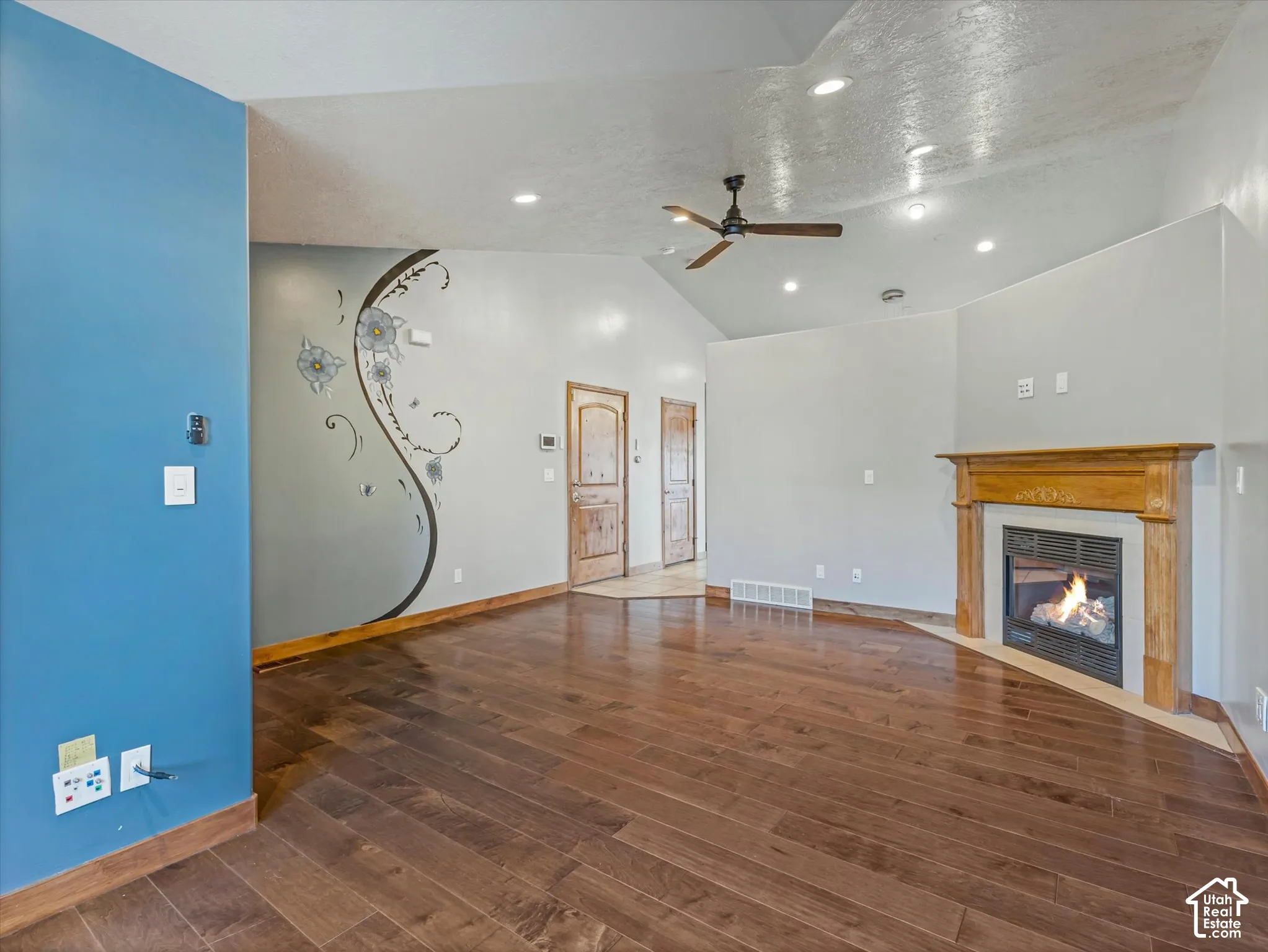 Dark wood-finish flooring, vaulted ceilings, recessed lighting, ceiling fan, and a fireplace with a wood mantle