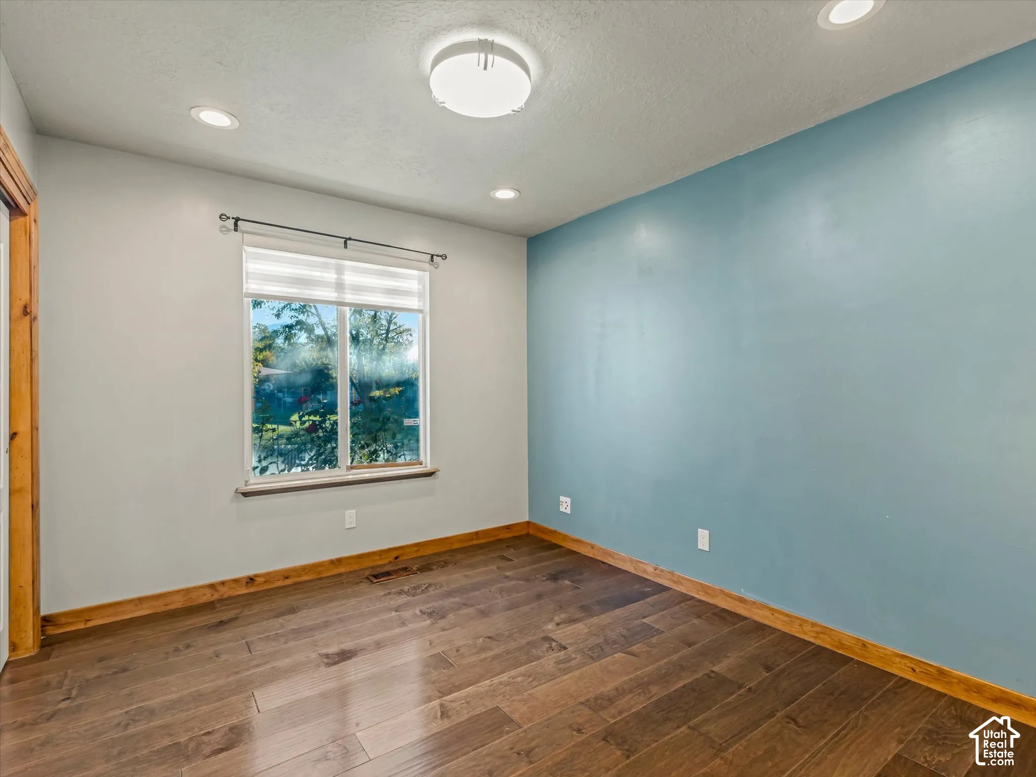 Wood-finish flooring, recessed lighting, central ceiling light fixture, window with blinds, and contrasting accent wall