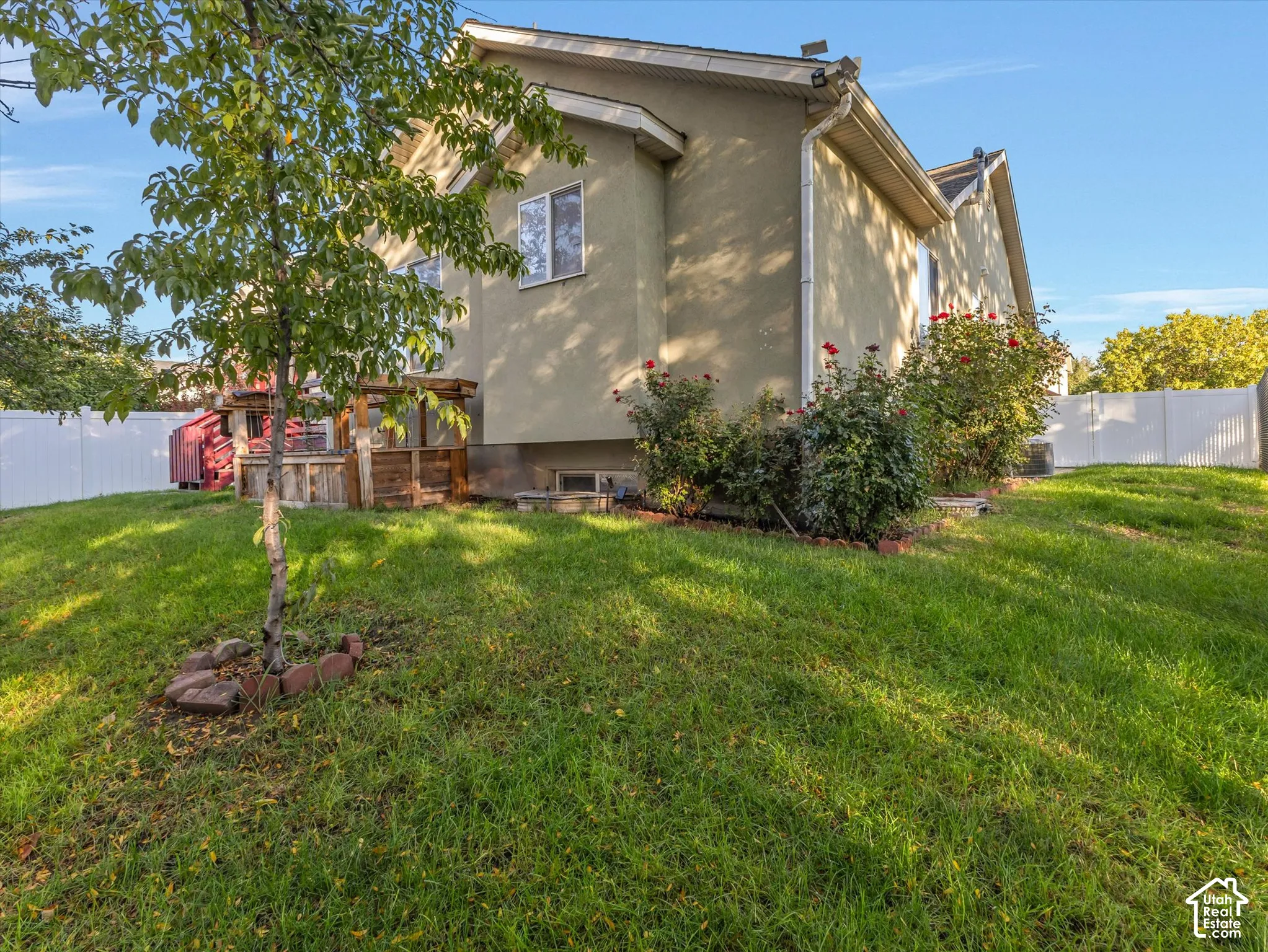 Stucco exterior with multiple windows, surrounded by green lawn and mature landscaping