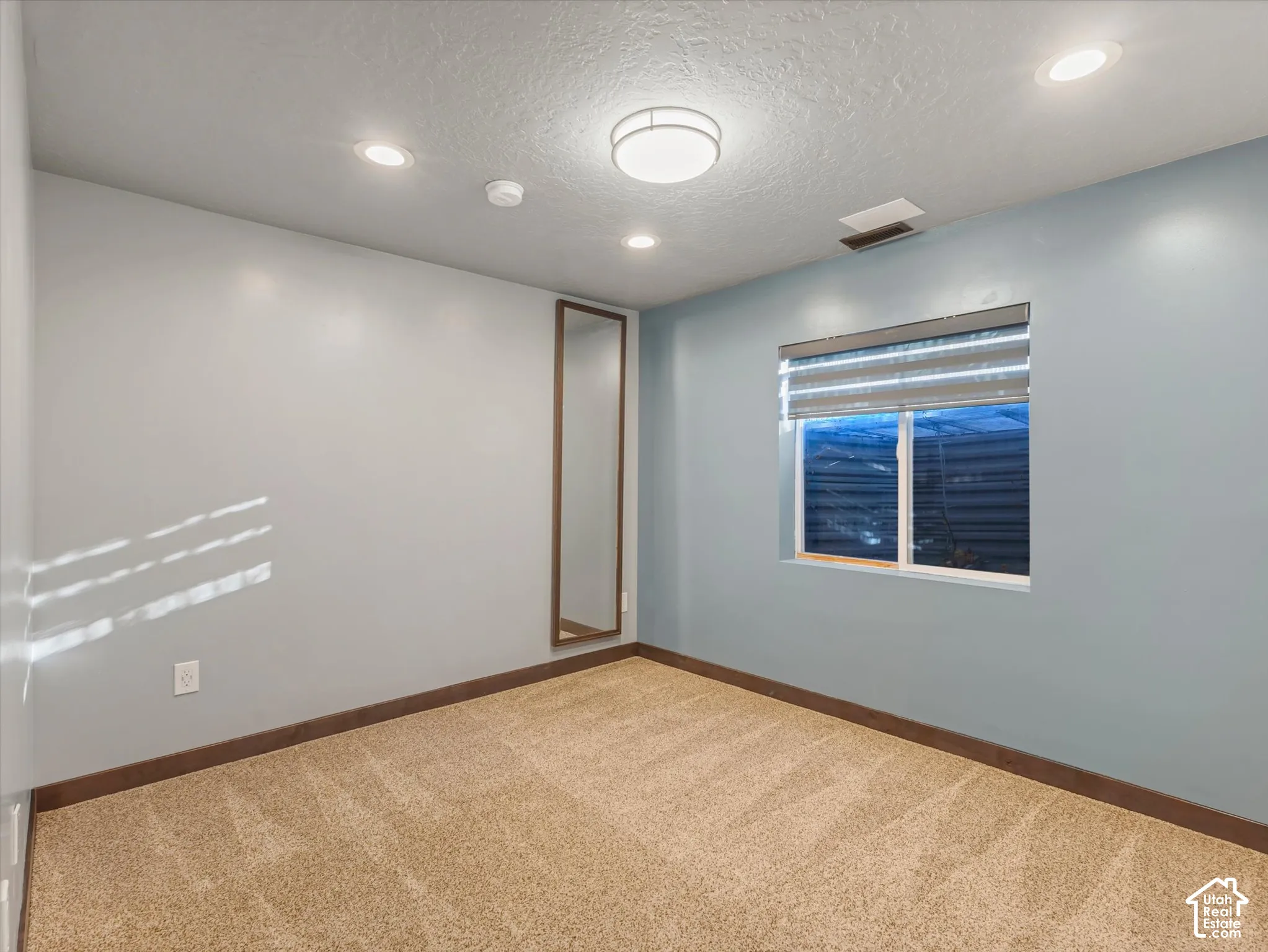 Recessed ceiling lighting, flush-mount ceiling light fixture, window with blinds, and neutral carpet